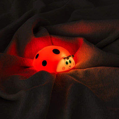 Glowing red ladybug-shaped night light on dark fabric