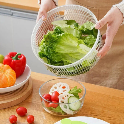 Person holding a salad spinner with lettuce over a wooden table with vegetables.