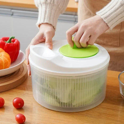 Person using a salad spinner with vegetables on a wooden table
