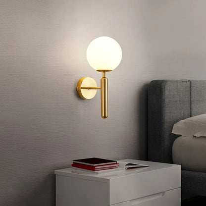 Modern wall sconce with a round light fixture on a gray wall next to a bed.