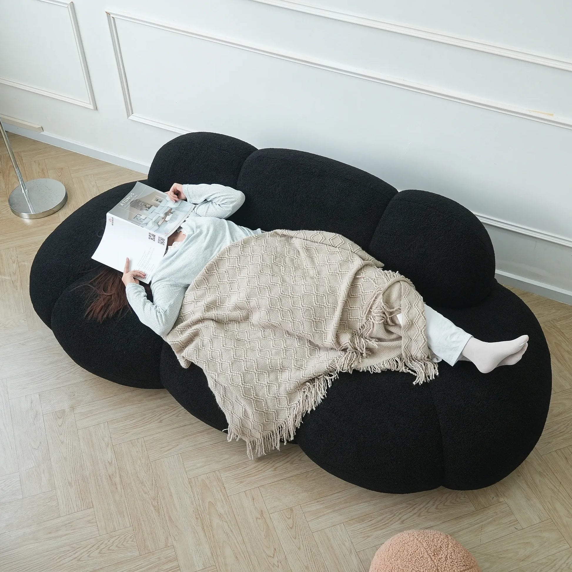 Person lying on a unique black bean-shaped sofa reading a newspaper.