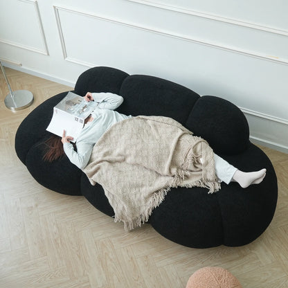 Person lying on a unique black bean-shaped sofa reading a newspaper.