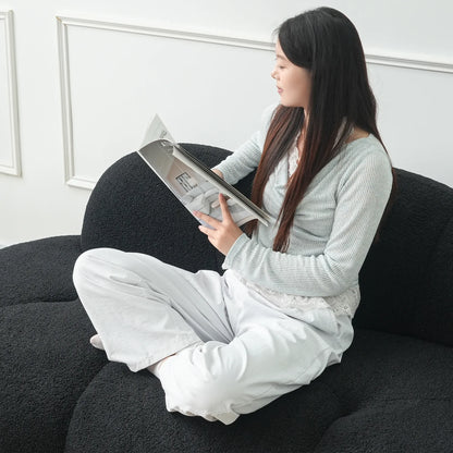 Woman sitting on a black sofa reading a magazine in a minimalistic room.