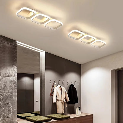 Modern ceiling lights in a hallway with coats hanging on hooks.