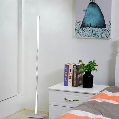 Modern floor lamp on a nightstand with books and a plant in a bedroom setting.