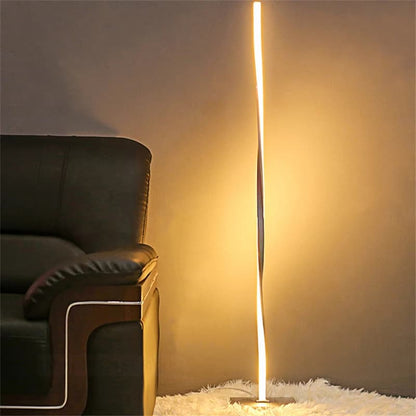 Modern floor lamp casting light on a wall next to a dark sofa.