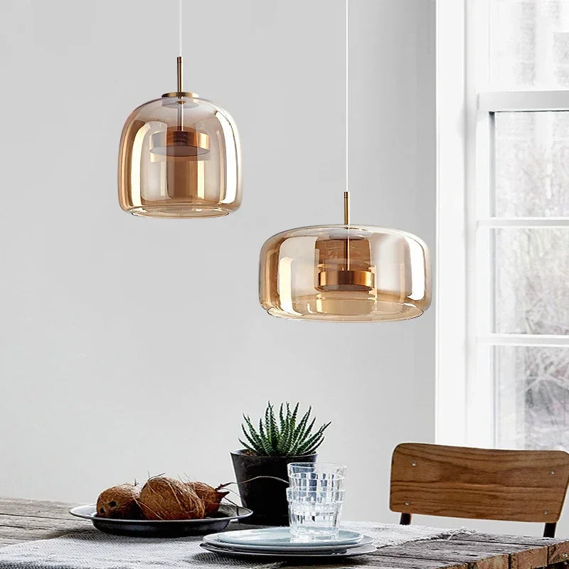 Two amber glass pendant lights hanging above a dining table with a plant and glasses.
