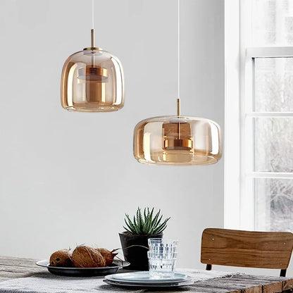 Two amber glass pendant lights hanging above a dining table with a plant and glasses.