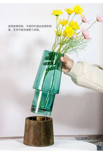 Person holding a green vase with flowers against a plain background
