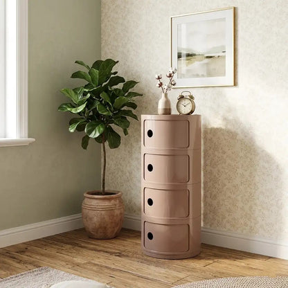 Pink cylindrical storage cabinet with drawers next to a potted plant in a room with a window and framed picture on the wall.