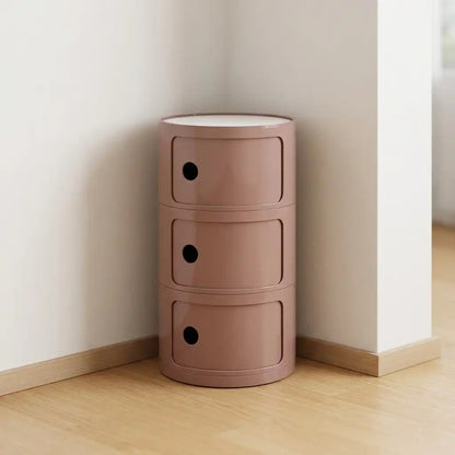 Pink cylindrical storage unit with three drawers against a white wall.