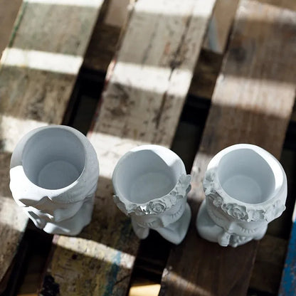 Three white ceramic planters with decorative designs on a wooden surface