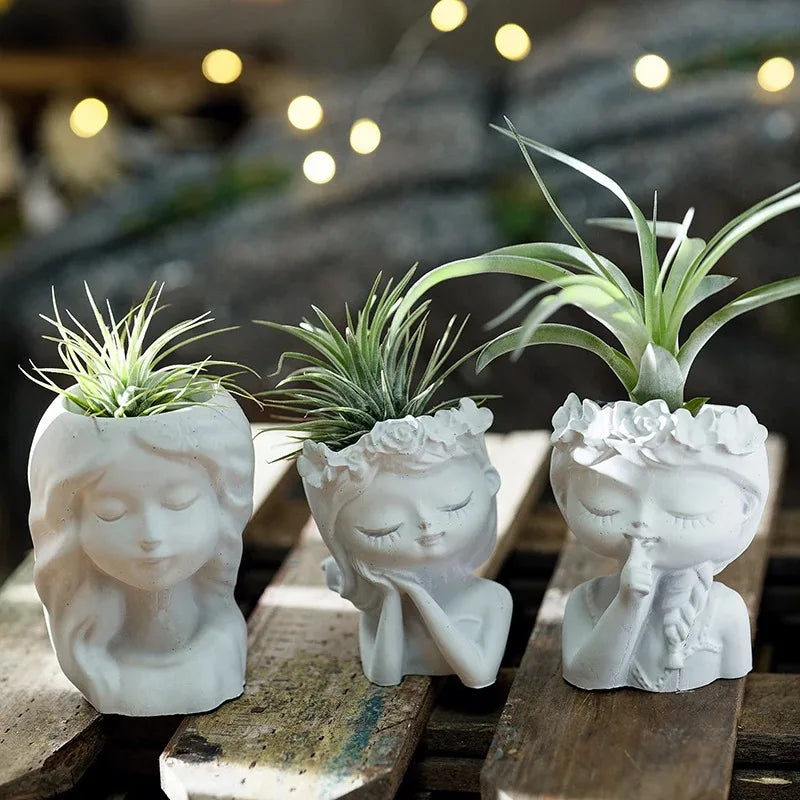 Three white ceramic planters shaped like faces on a wooden surface with blurred lights in the background.