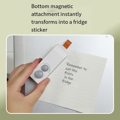 Hand holding a magnetic attachment device with text on a fridge door.