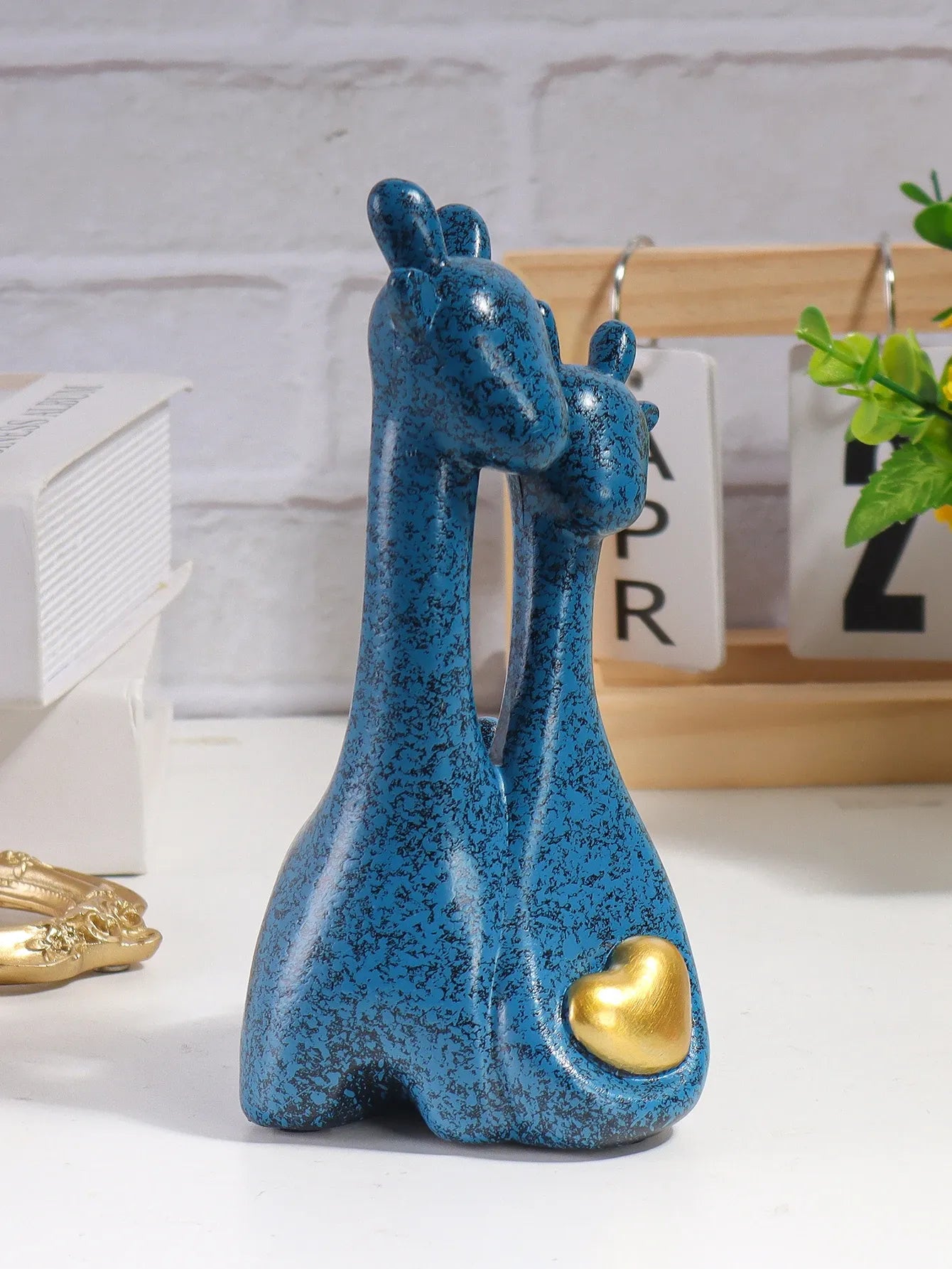 Blue ceramic giraffe figurine with a gold heart on a white surface.