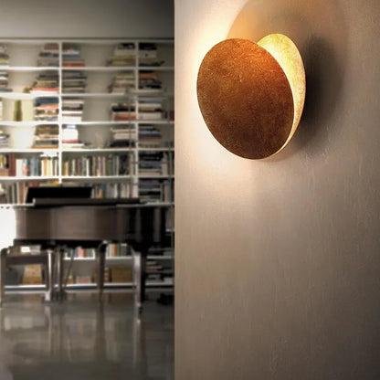 Round wall light fixture on a wall with a bookshelf and piano in the background