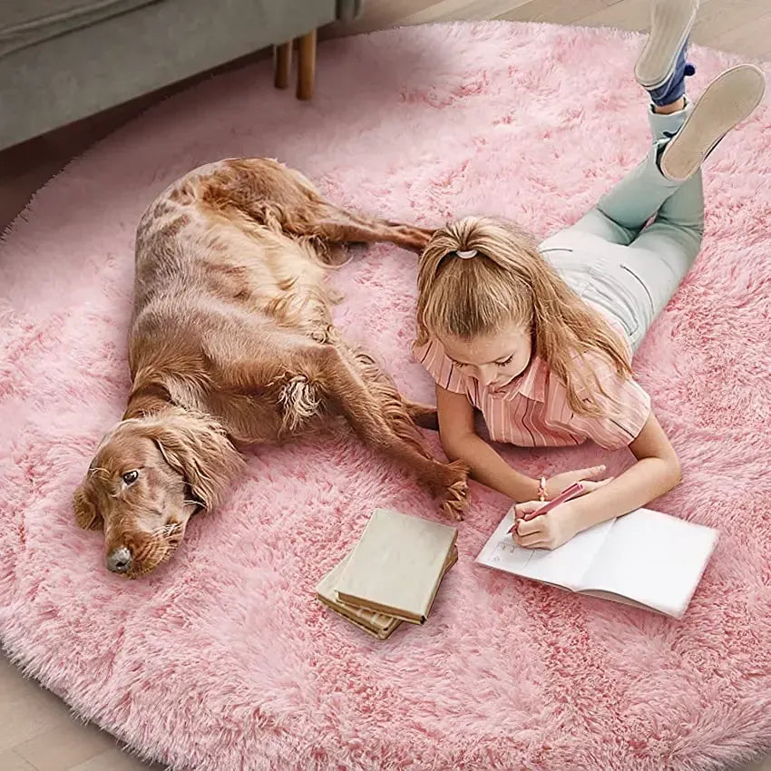 Girl lying on a pink rug with a dog, reading a book.