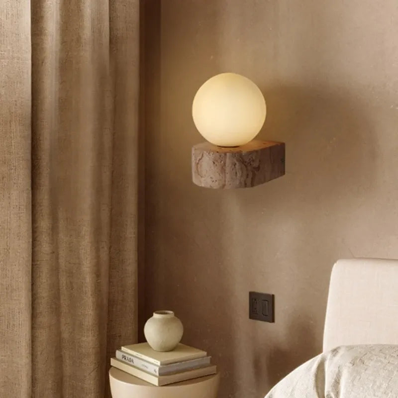 Spherical wall light fixture on a textured wall with books and a vase below.