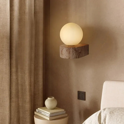 Spherical wall light fixture on a textured wall with books and a vase below.