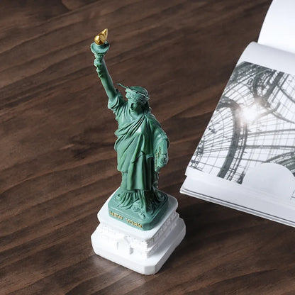 Statue of Liberty figurine on a wooden surface with a book in the background