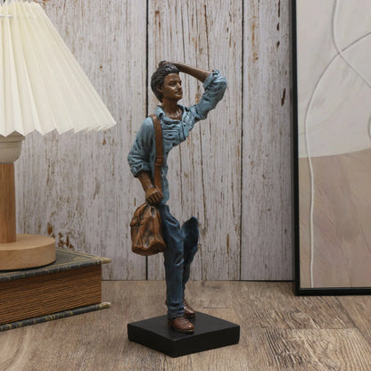 Statue of a person with a bag and umbrella on a wooden floor with a lamp and books in the background.