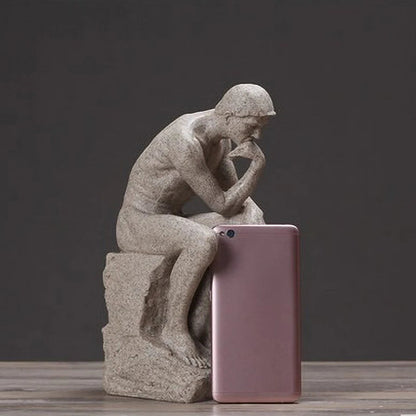 Statue of a thinker next to a pink smartphone on a wooden surface with a dark background