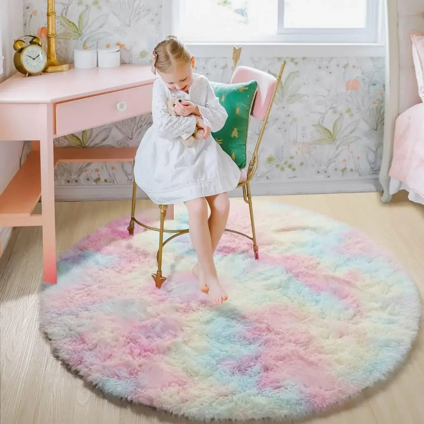 Child sitting on a colorful round rug in a room with a desk and chair.