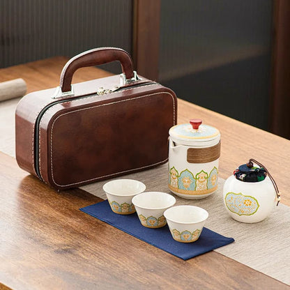 Tea set with a ceramic teapot, cups, and a brown leather case on a wooden table.