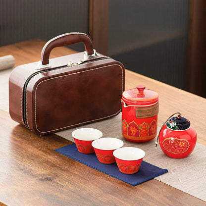 Tea set with red teacups and teapot, brown suitcase on a wooden table