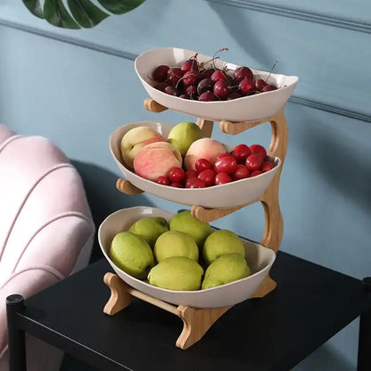 Three-tiered fruit basket with apples, pears, and cherries on a black surface against a blue wall.