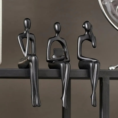Three black metal sculptures of people sitting on a surface against a dark background