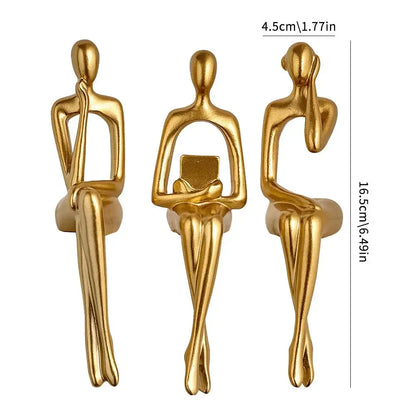 Three gold-colored sculptures of sitting figures with measurements on a white background