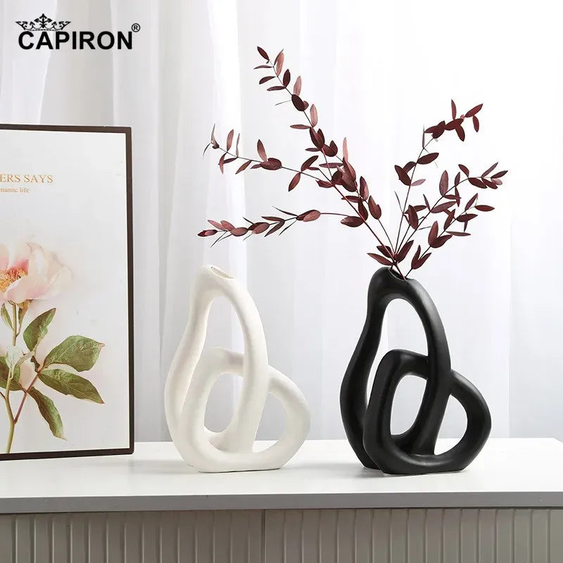 Two decorative vases, one white and one black, on a surface with a framed picture in the background.