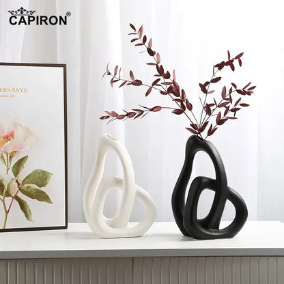Two decorative vases, one white and one black, on a surface with a framed picture in the background.