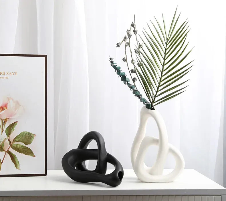 Two abstract ceramic sculptures on a surface with a framed picture of flowers in the background.