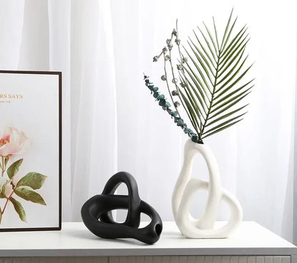 Two abstract ceramic sculptures on a surface with a framed picture of flowers in the background.