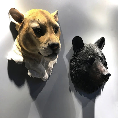 Two animal head sculptures, one resembling a lion and the other a bear, on a white wall.