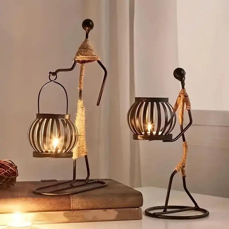 Two decorative candle holders shaped like people on a wooden surface with a neutral background.