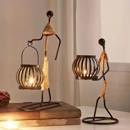 Two decorative candle holders shaped like people on a wooden surface with a neutral background.