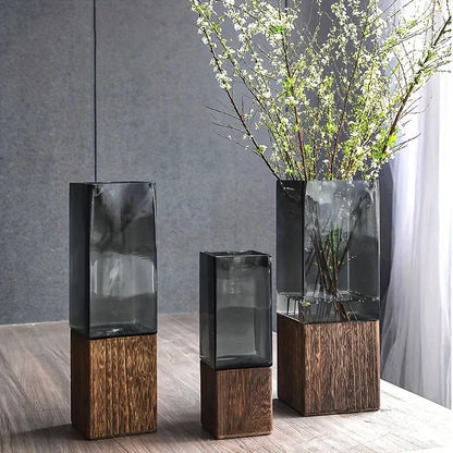 Two glass vases with wooden bases on a wooden floor against a gray wall.