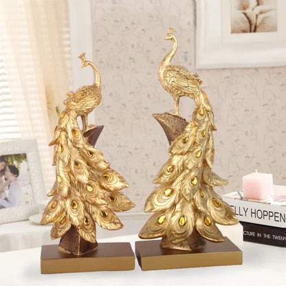 Two gold peacock sculptures on a surface with a blurred background