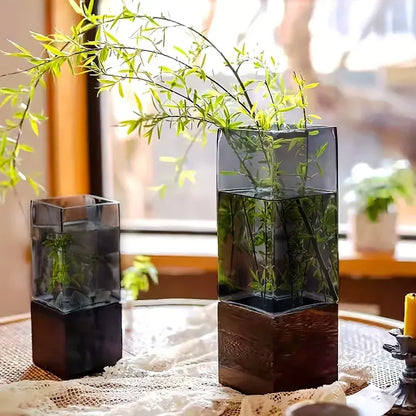 Two square glass vases with water and green plants on a lace tablecloth.