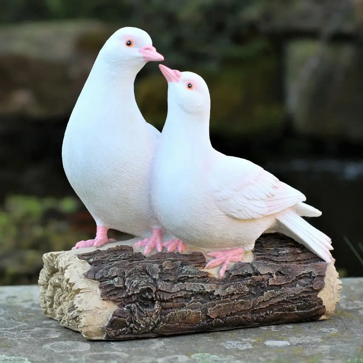 Two white pigeon sculptures on a wooden log with a natural background
