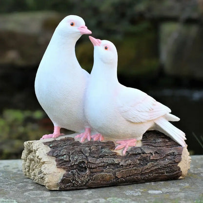 Two white pigeon sculptures on a wooden log with a natural background
