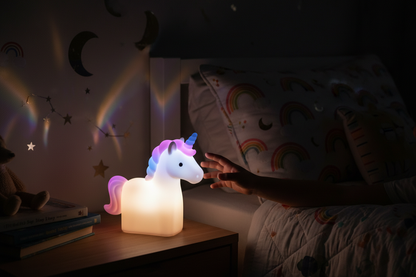 Palm-sized unicorn LED nightlight glowing softly in a dark child's bedroom with warm multicolor light