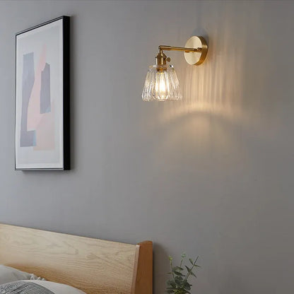Wall-mounted lamp with glass shade on a gray wall above a bed.