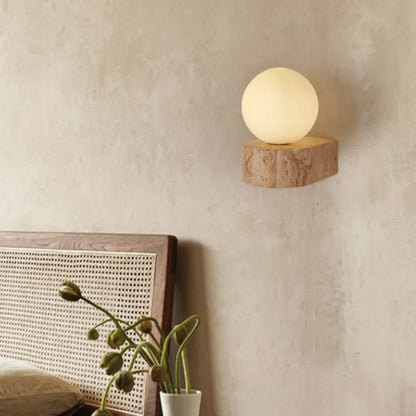Wall-mounted light fixture on a textured wall with a plant and headboard in the foreground.