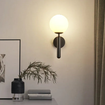 Wall-mounted light fixture on a wall with a plant and framed picture in the foreground.