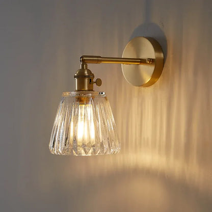 Wall-mounted light fixture with a glass shade and a brass arm on the wall.