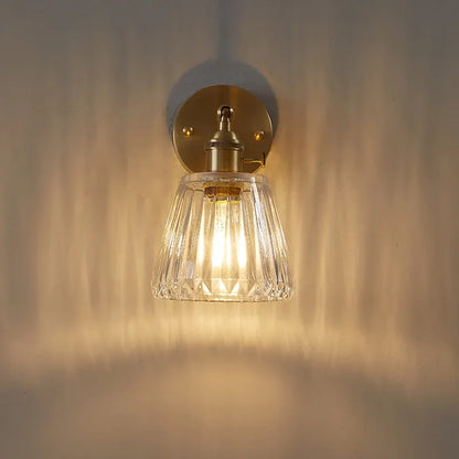 Wall-mounted light fixture with clear glass shade and gold metal fixture on a neutral background